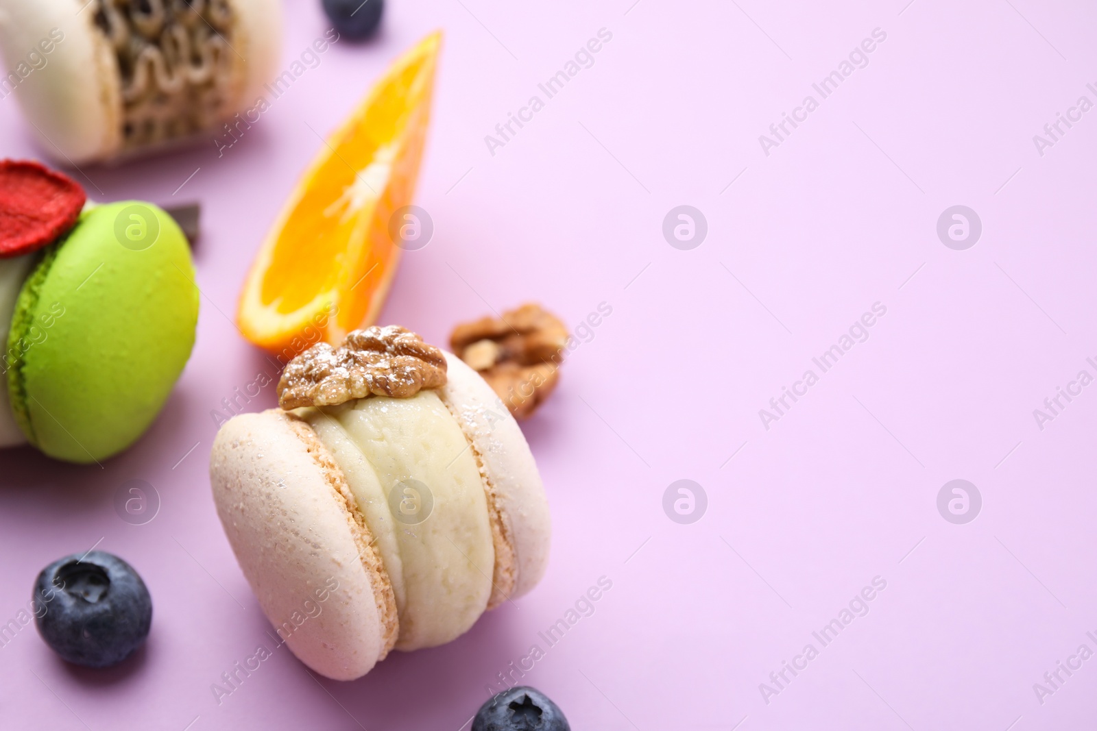 Photo of Delicious macarons, orange and berries on violet table, closeup. Space for text