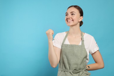 Photo of Beautiful young woman in clean apron with pattern on light blue background. Space for text