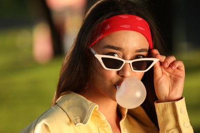 Photo of Beautiful young woman in sunglasses blowing bubble gum in park