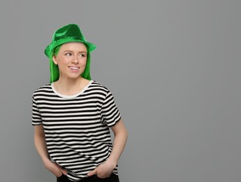 Image of St. Patrick's day party. Pretty woman with green hair and leprechaun hat on grey background. Space for text