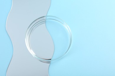 Empty petri dish and mirror on light blue background, flat lay. Space for text