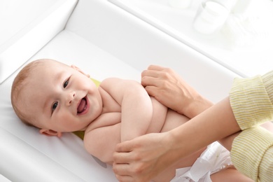 Photo of Young woman massaging cute baby on changing table