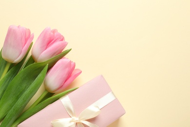 Photo of Beautiful spring tulips and gift box on color background, top view with space for text. International Women's Day