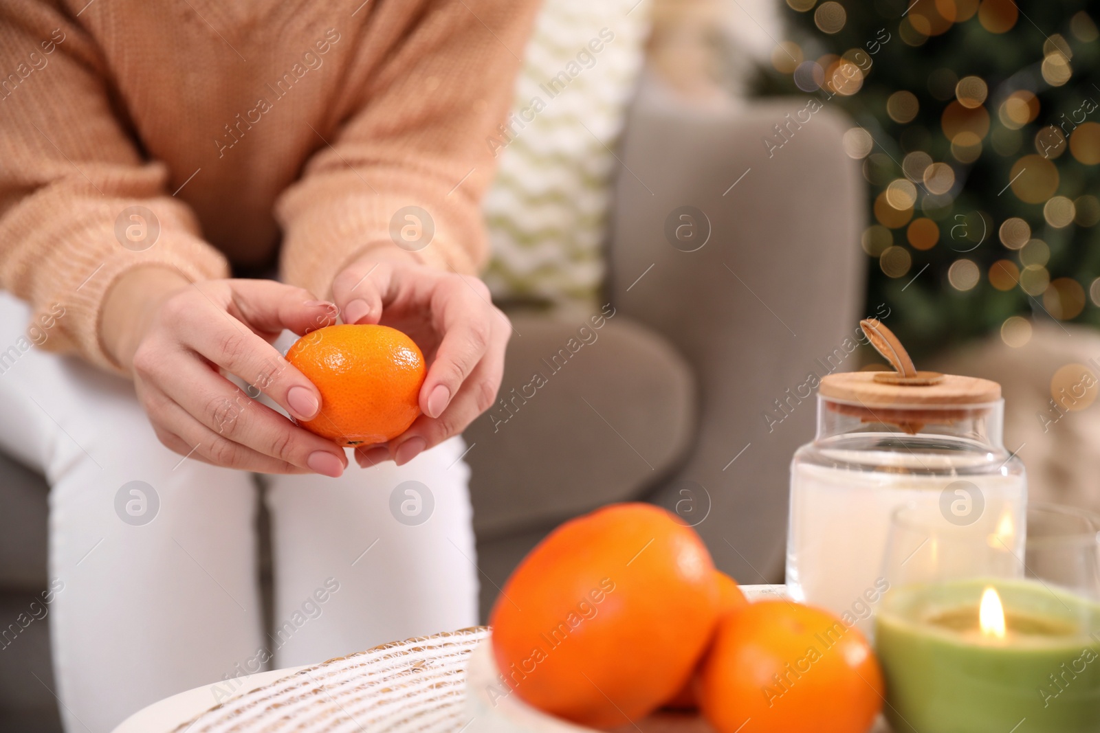 Photo of Young woman peeling fresh tangerine on sofa indoors, closeup