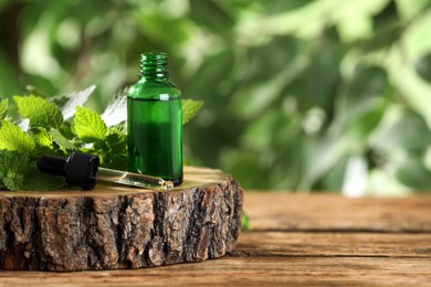 Photo of Glass bottle of nettle oil with dropper and fresh leaves on wooden table against blurred background, space for text