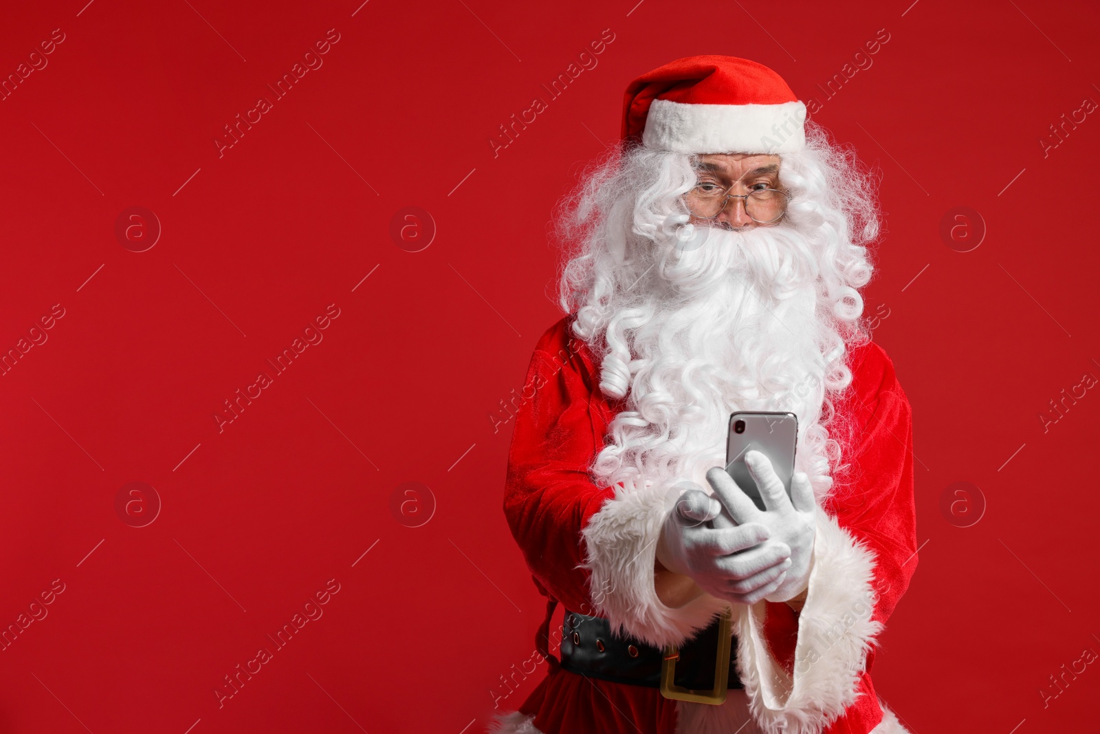 Photo of Merry Christmas. Santa Claus using smartphone on red background, space for text