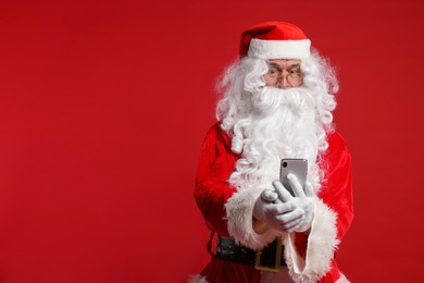 Merry Christmas. Santa Claus using smartphone on red background, space for text