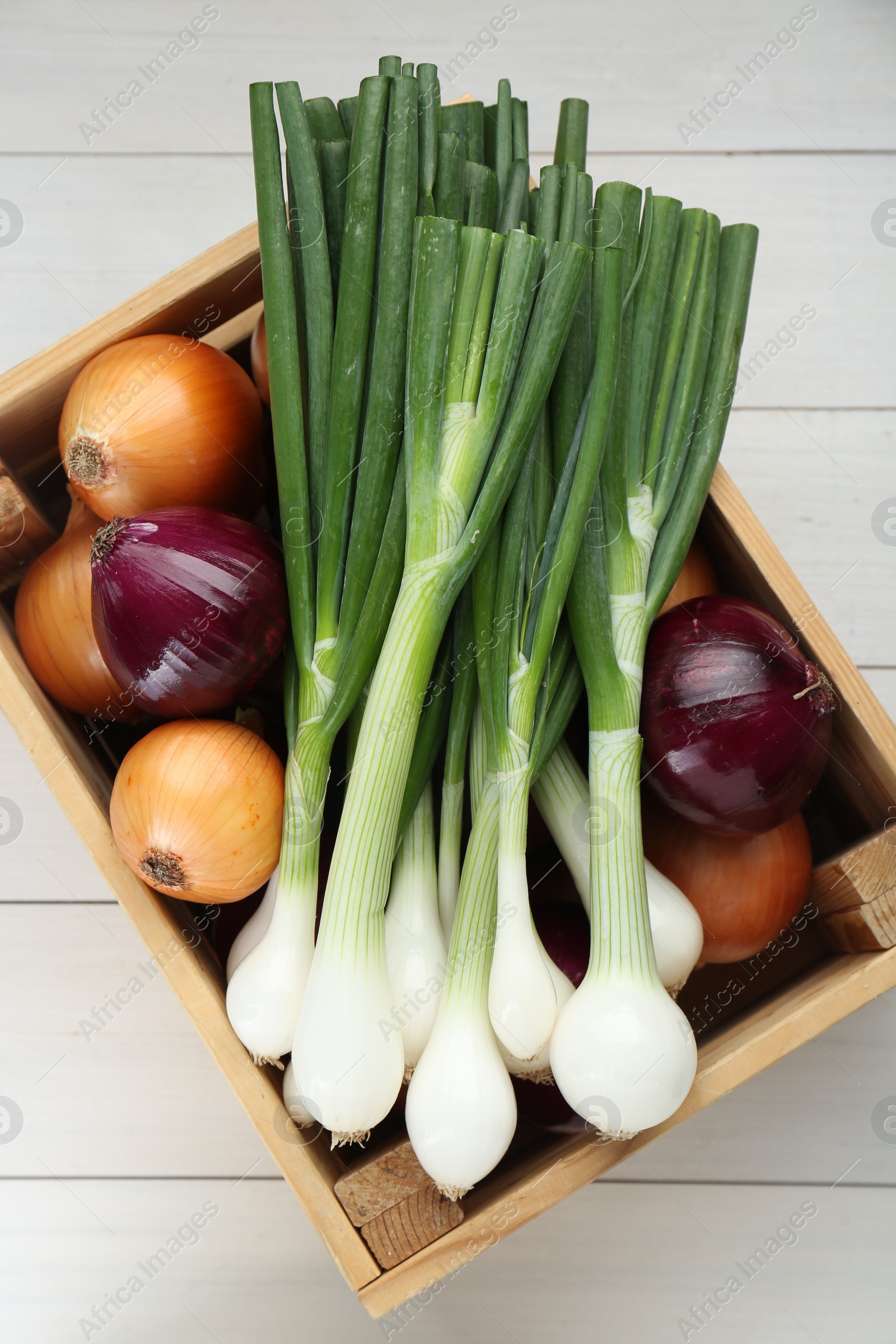 Photo of Crate with different kinds of onions on white wooden table, top view