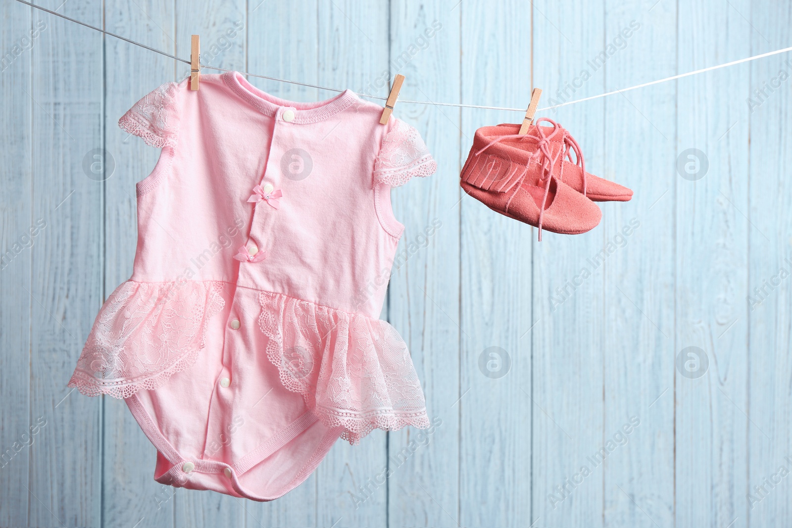 Photo of Pair of shoes and bodysuit on laundry line against wooden background. Baby accessories