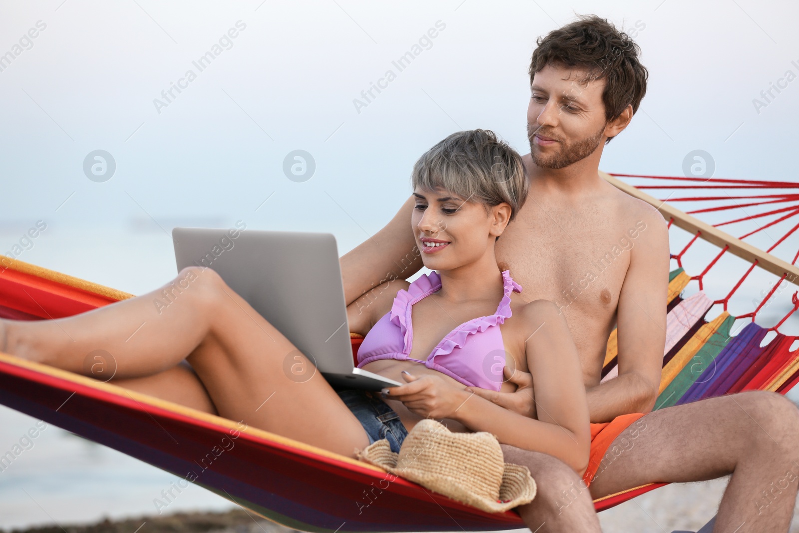 Photo of Young couple resting with laptop in hammock on beach