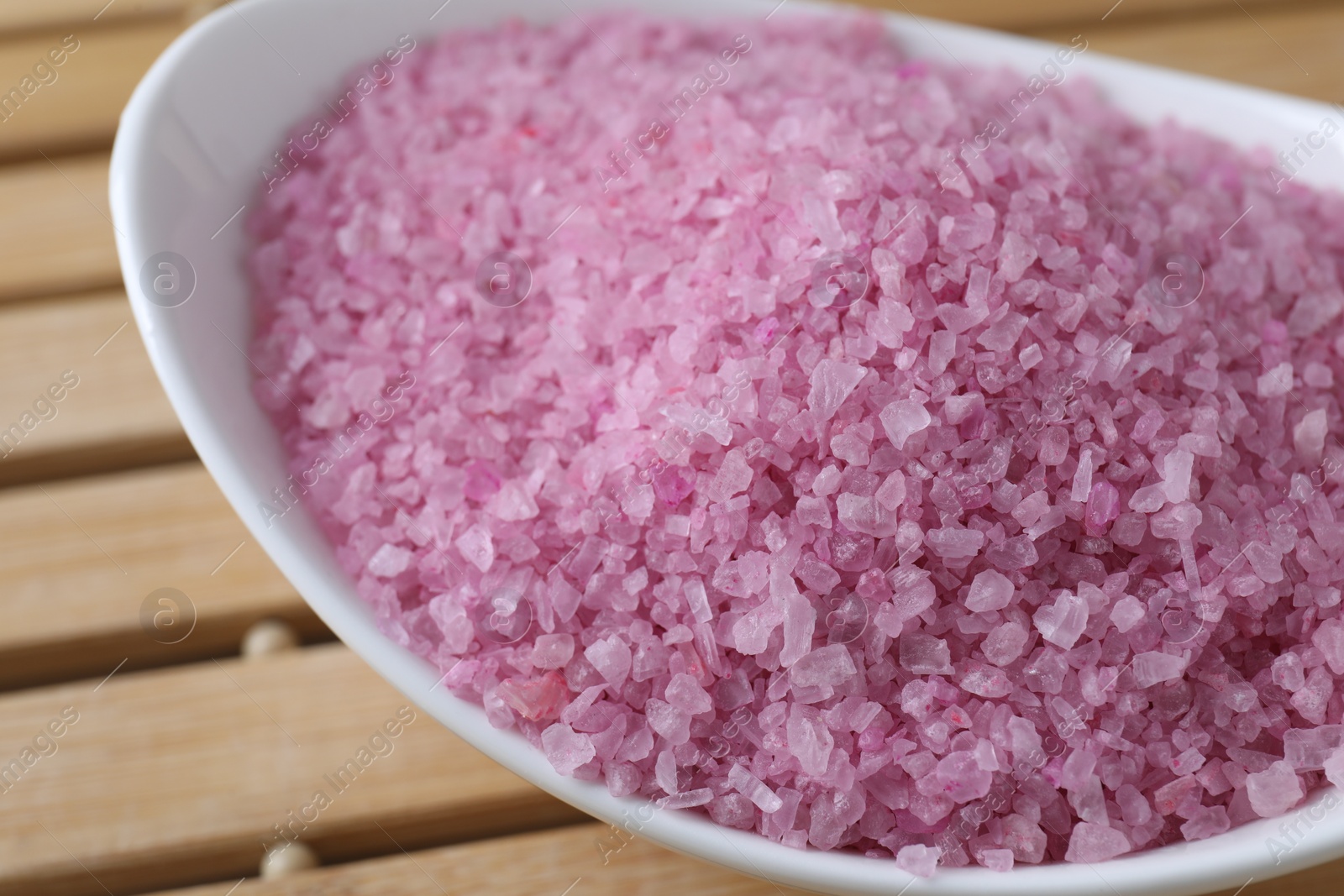Photo of Bowl with pink sea salt on wooden table, closeup