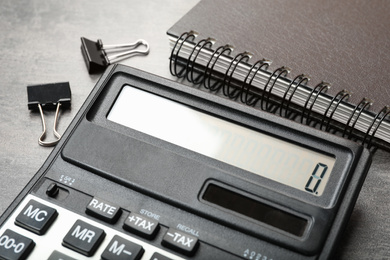Photo of Calculator, notebook and paper clips on grey table, closeup. Tax accounting