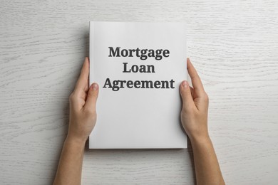 Image of Woman holding mortgage loan agreement on white wooden table, top view