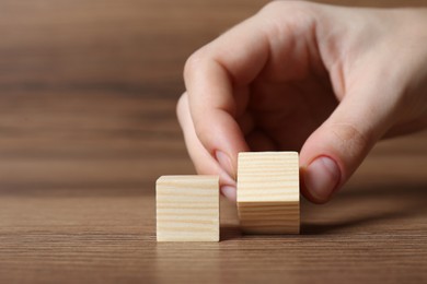 Photo of Woman arranging cubes on wooden background, closeup with space for text. Idea concept