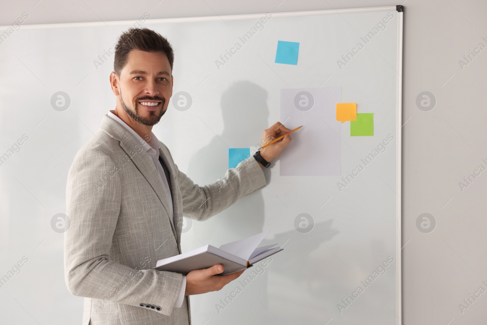 Photo of Happy teacher with book explaining something at whiteboard in classroom