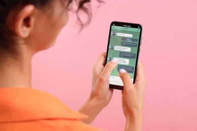 Image of Woman texting with friend using messaging application on smartphone against pink background, closeup