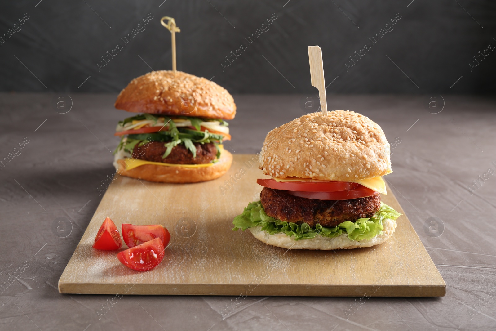 Photo of Board with delicious vegetarian burgers on grey textured table