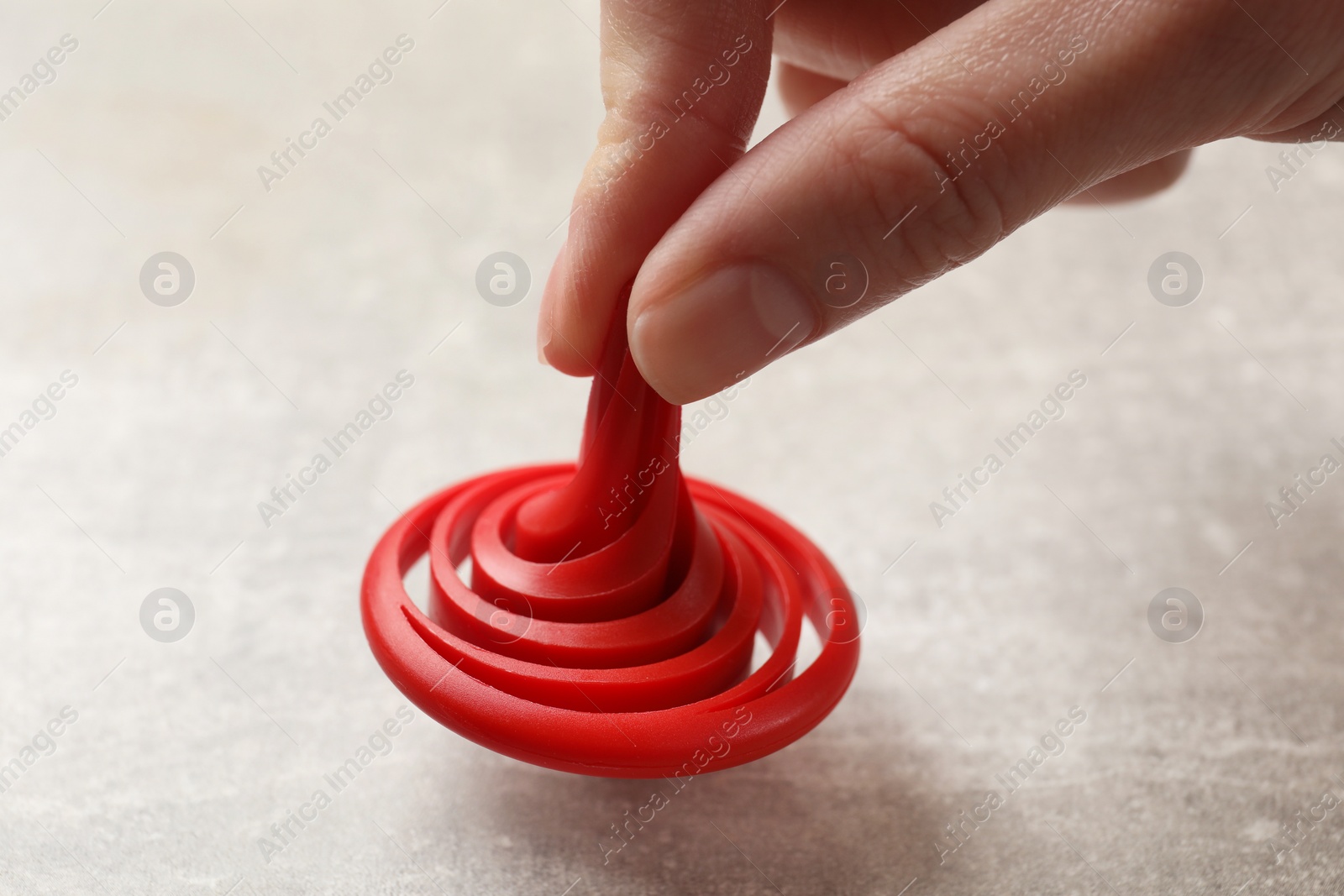 Photo of Woman playing with red spinning top at grey textured background, closeup