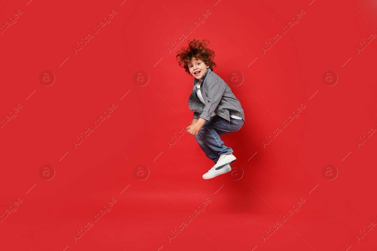 Photo of Happy little boy dancing on red background. Space for text