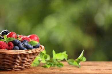 Photo of Wicker bowl with different fresh ripe berries and mint on wooden table outdoors, space for text