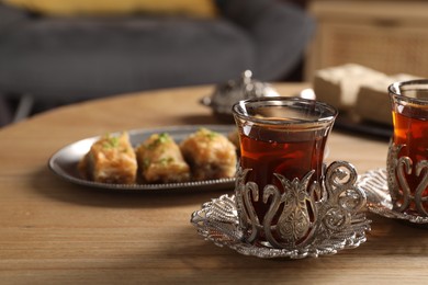 Photo of Glasses of traditional Turkish tea in vintage holders and fresh baklava on wooden table. Space for text