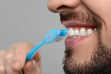 Photo of Man brushing his teeth with plastic toothbrush on light grey background, closeup