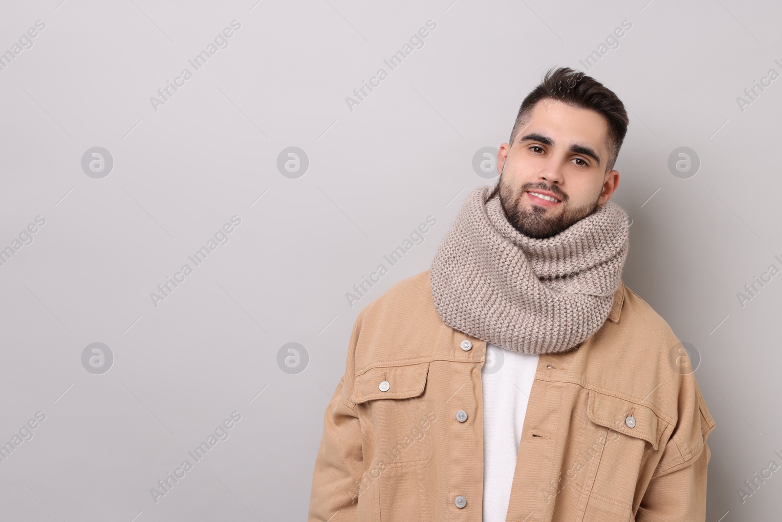 Photo of Smiling man in warm scarf on light grey background. Space for text