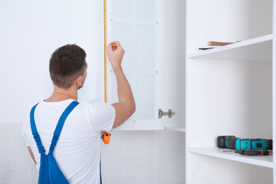 Photo of Worker measuring newly installed kitchen furniture indoors