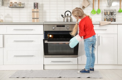 Little girl baking buns in oven at home