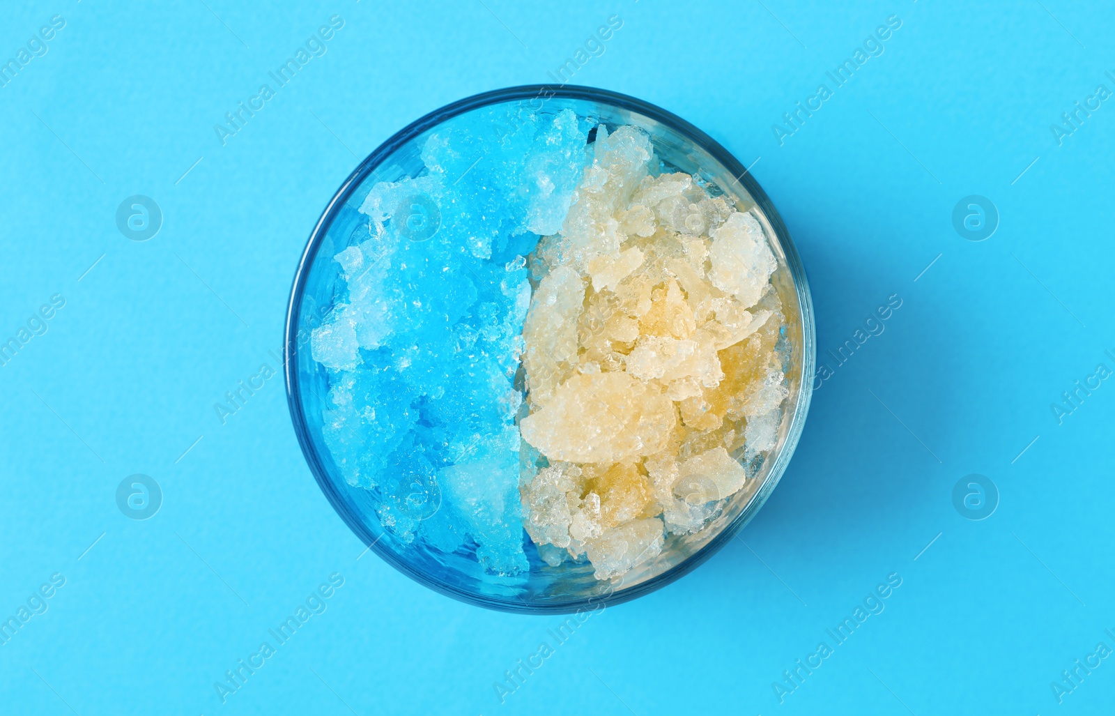 Photo of Rainbow shaving ice in glass dessert bowl on light blue background, top view