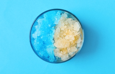 Rainbow shaving ice in glass dessert bowl on light blue background, top view