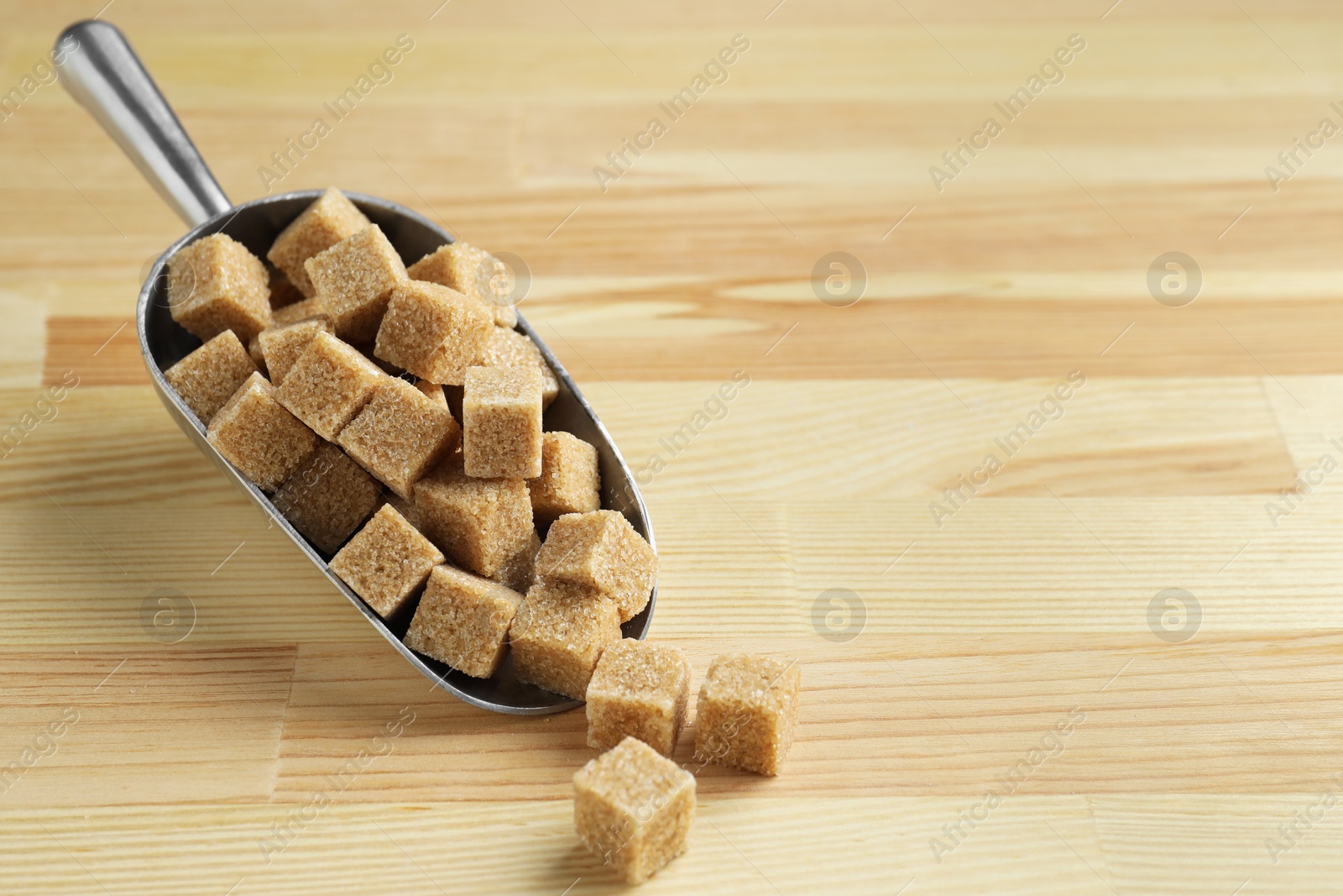 Photo of Brown sugar cubes in scoop on wooden table, closeup. Space for text