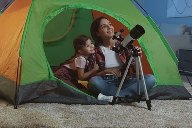 Photo of Happy mother and her daughter using telescope to look at stars while sitting in camping tent indoors