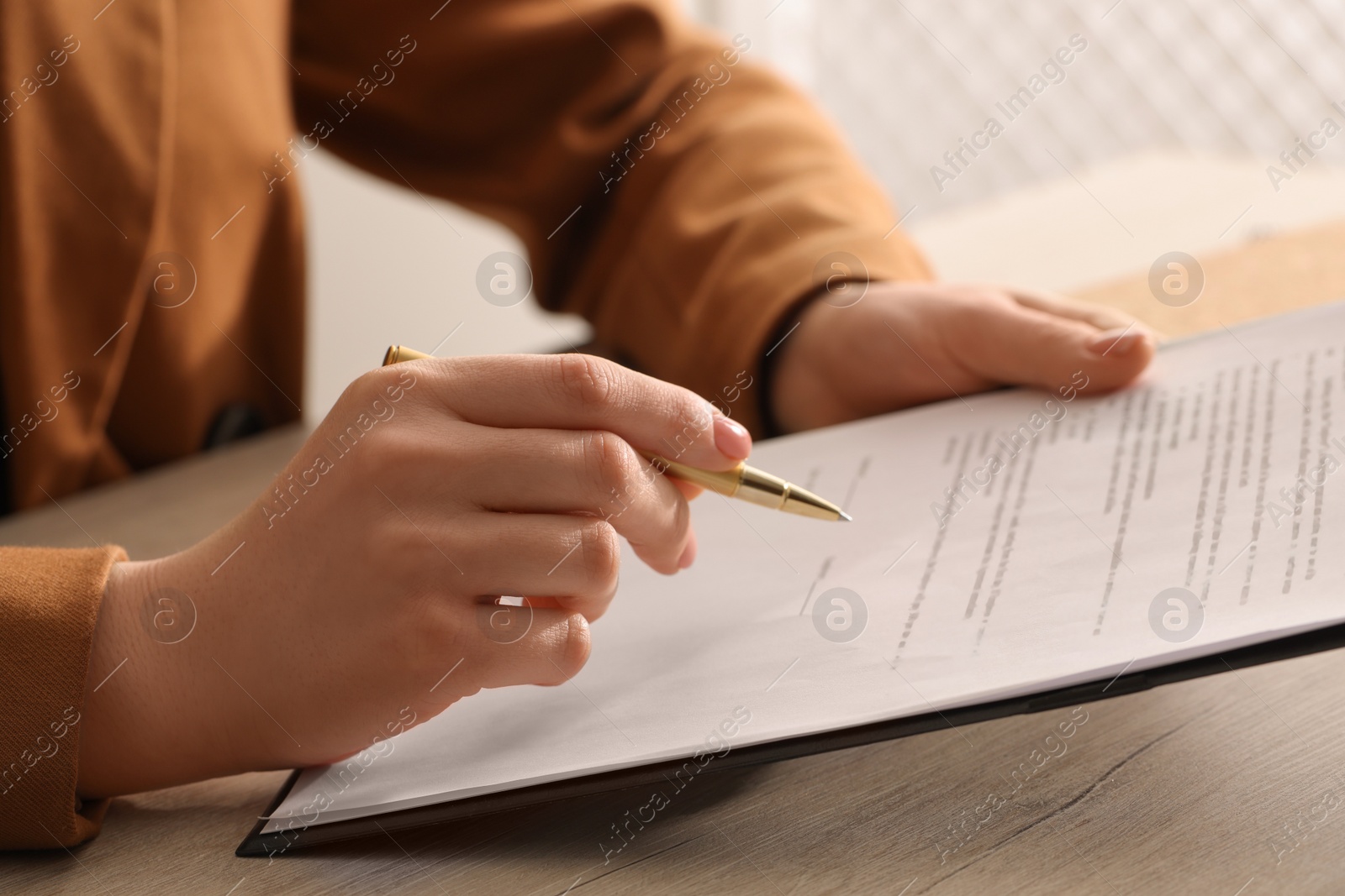 Photo of Woman signing document at wooden table, closeup