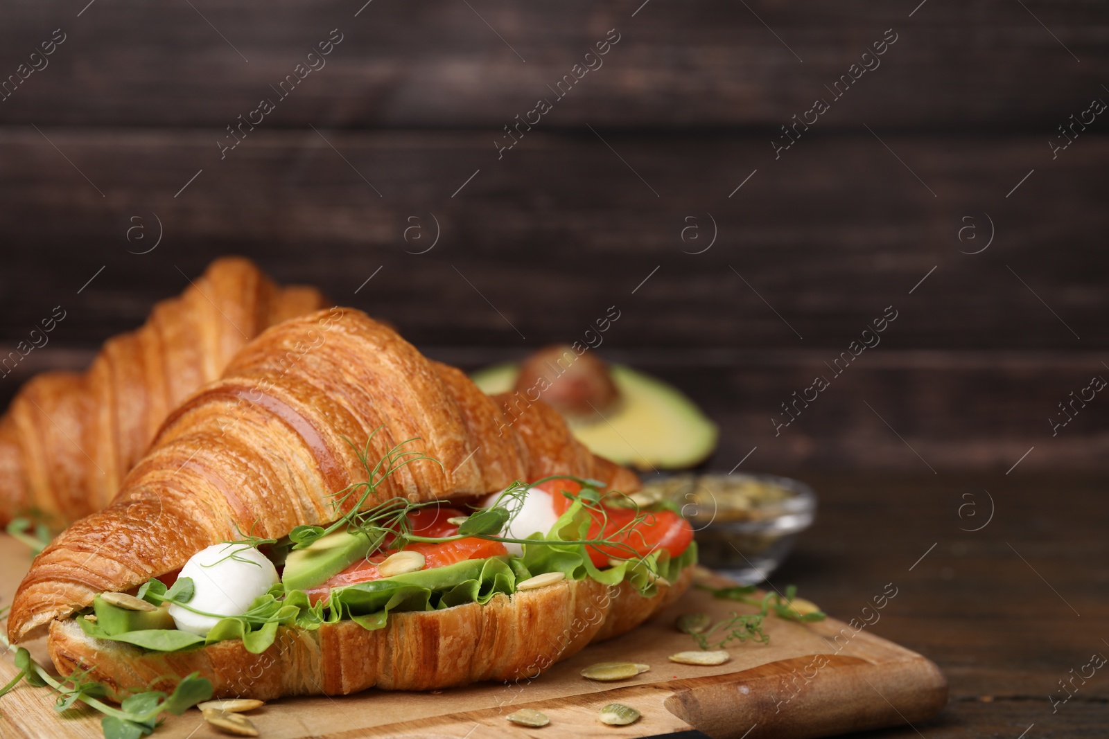 Photo of Tasty croissant with salmon, avocado, mozzarella and lettuce on wooden table, closeup. Space for text