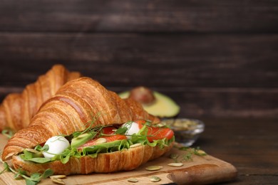 Tasty croissant with salmon, avocado, mozzarella and lettuce on wooden table, closeup. Space for text