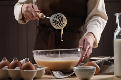 Woman making dough with whisk in bowl at table, closeup