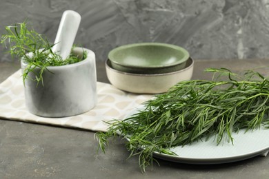 Photo of Plate and mortar with fresh tarragon leaves on grey table