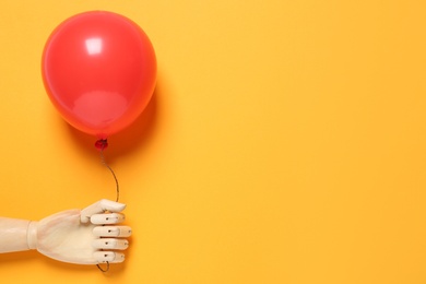 Photo of Wooden mannequin hand with red balloon on yellow background, space for text