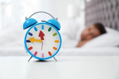 Photo of Analog alarm clock and blurred man on background. Time of day