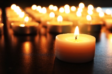 Photo of Wax candle burning on table in darkness, closeup