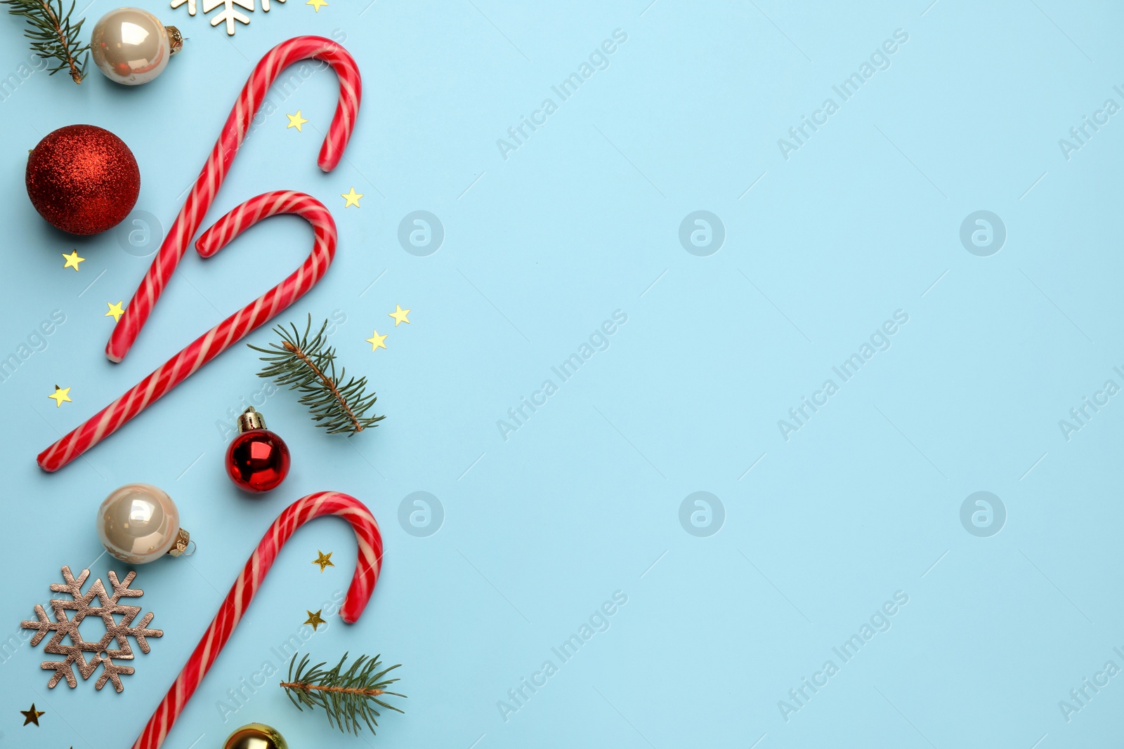 Photo of Flat lay composition with sweet candy canes and Christmas decor on light blue background, space for text