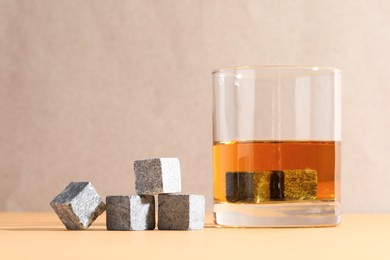 Whiskey stones and drink in glass on orange table, closeup. Space for text