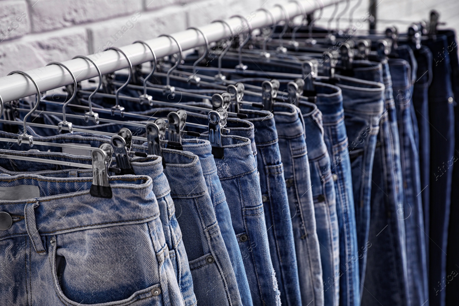 Photo of Rack with stylish jeans near brick wall, closeup