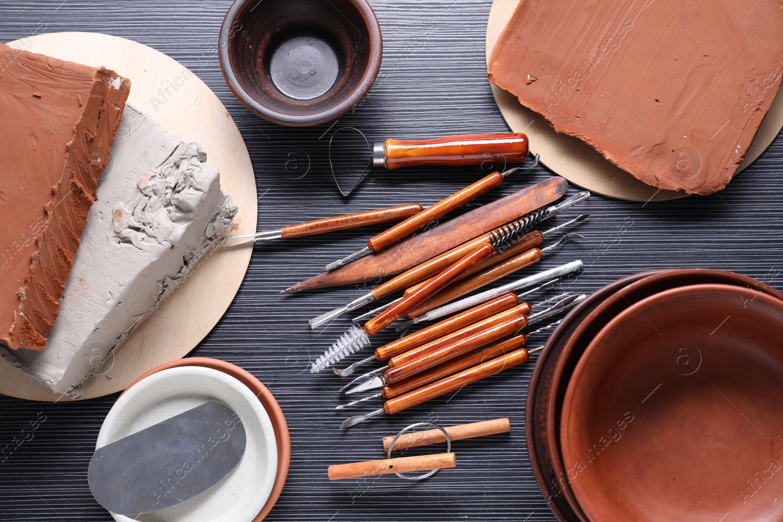 Photo of Clay, dishes and set of crafting tools on black table, flat lay