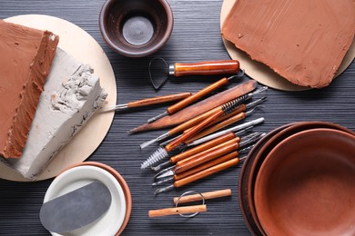 Clay, dishes and set of crafting tools on black table, flat lay