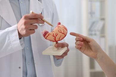 Photo of Gastroenterologist with human stomach model consulting patient in clinic, closeup
