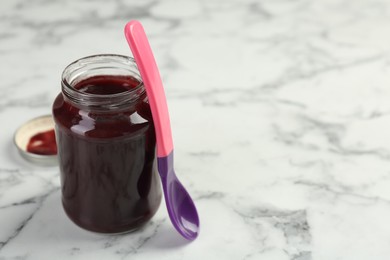 Tasty baby food in jar and spoon on white marble table, closeup. Space for text