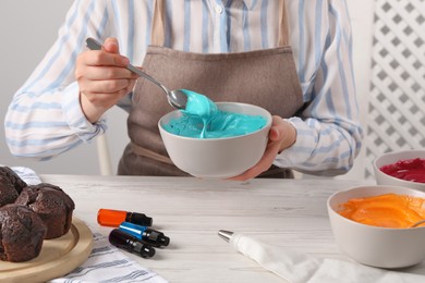 Woman mixing cream with light blue food coloring at white wooden table, closeup. Decorate cupcakes