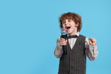 Cute little boy with microphone singing on light blue background, space for text
